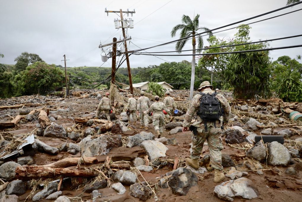 Soldiers walking through a disaster area with debris and damage visible
