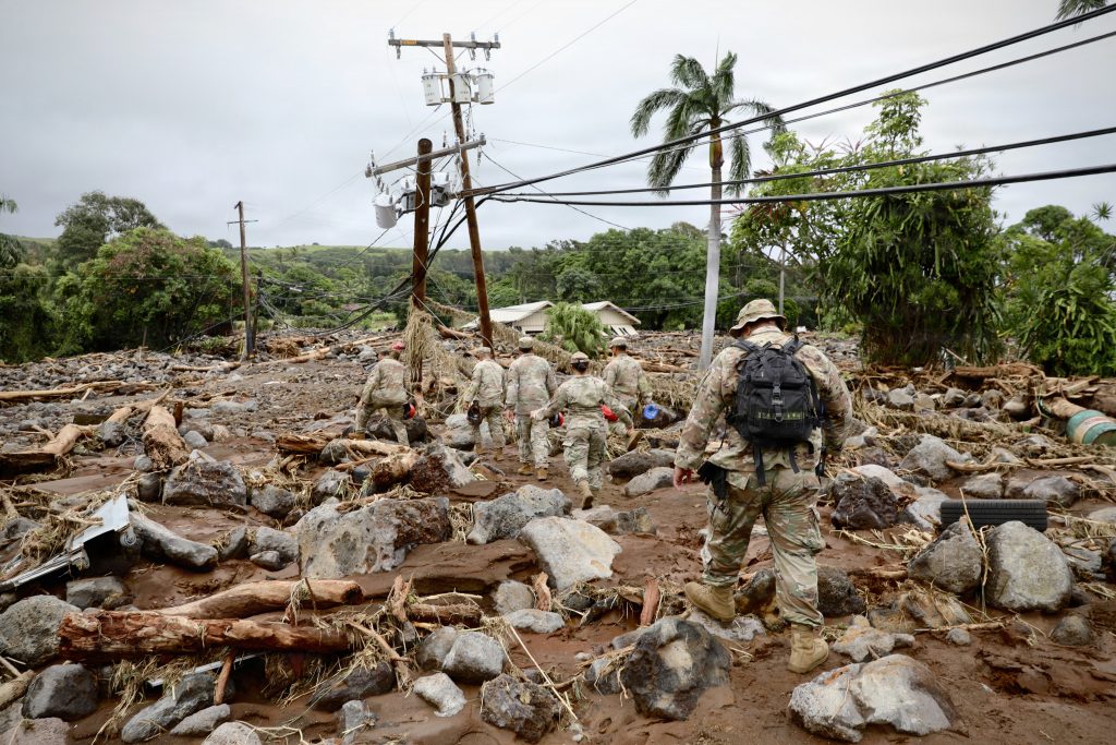 Soldiers walking through a disaster area with debris and damage visible